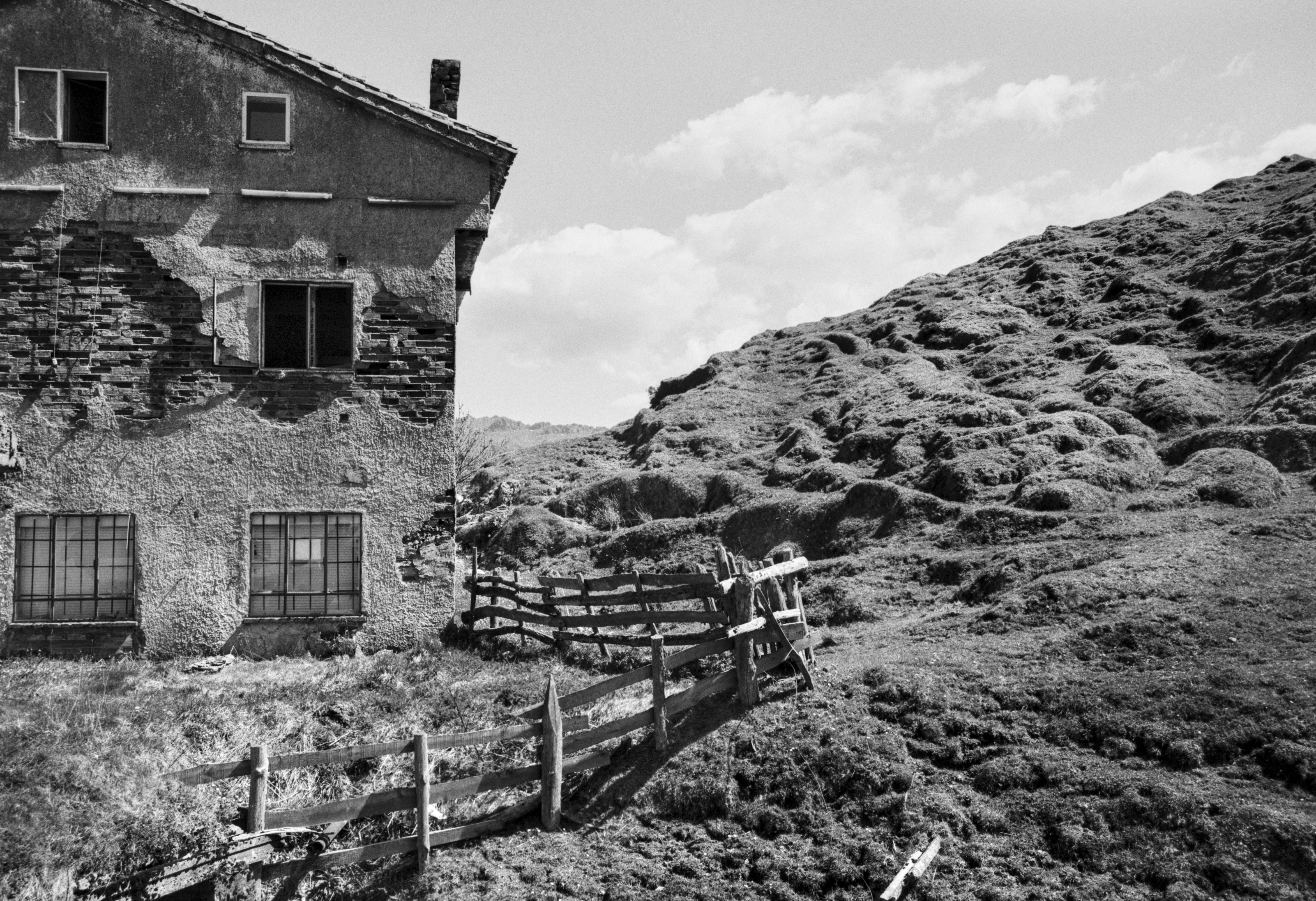 An old abandoned house in Arbas del Puerto beside a rugged hillside and a collapsed wooden fence.