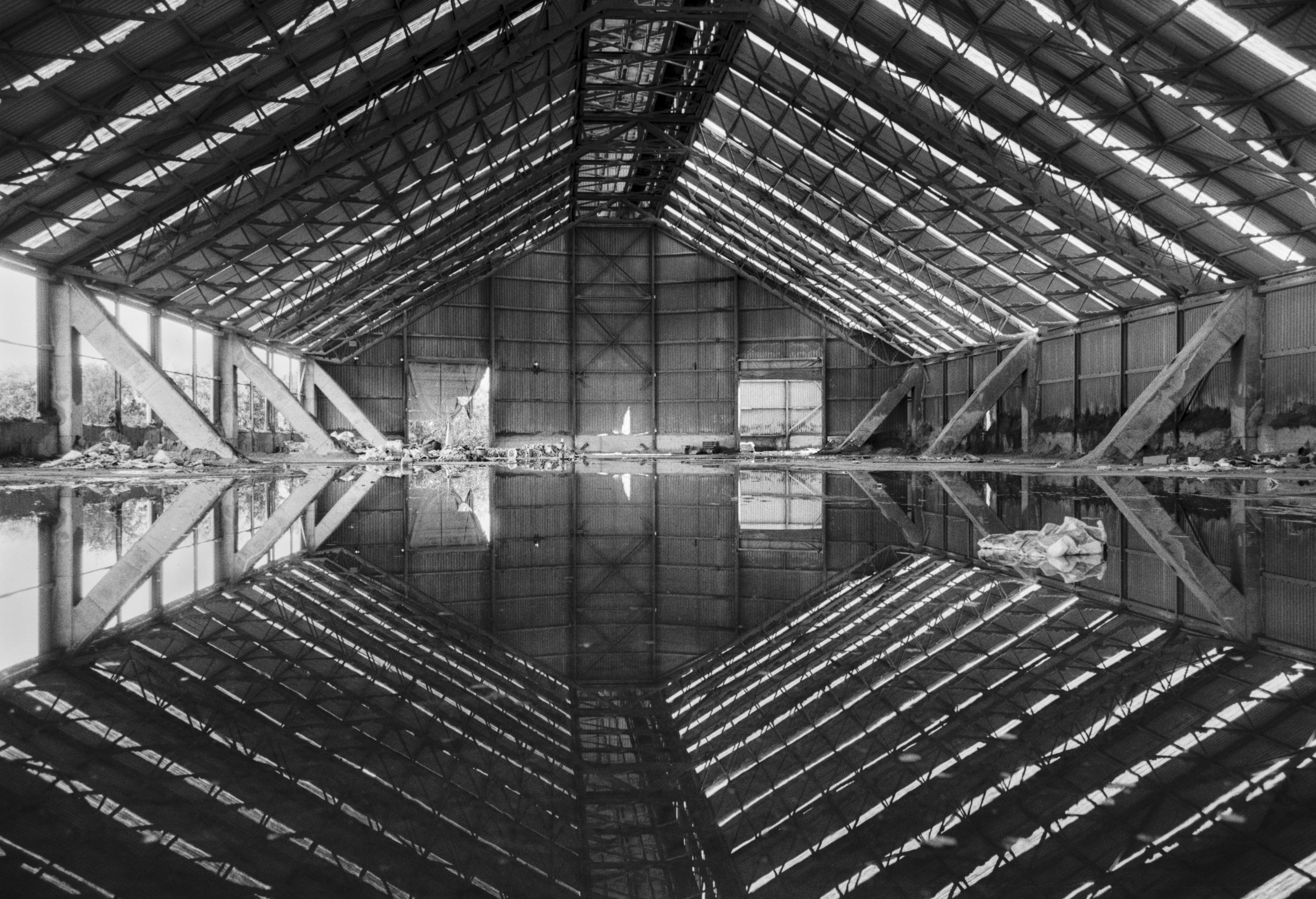 Interior of an abandoned industrial warehouse with its roof perfectly reflected in a flooded floor.
