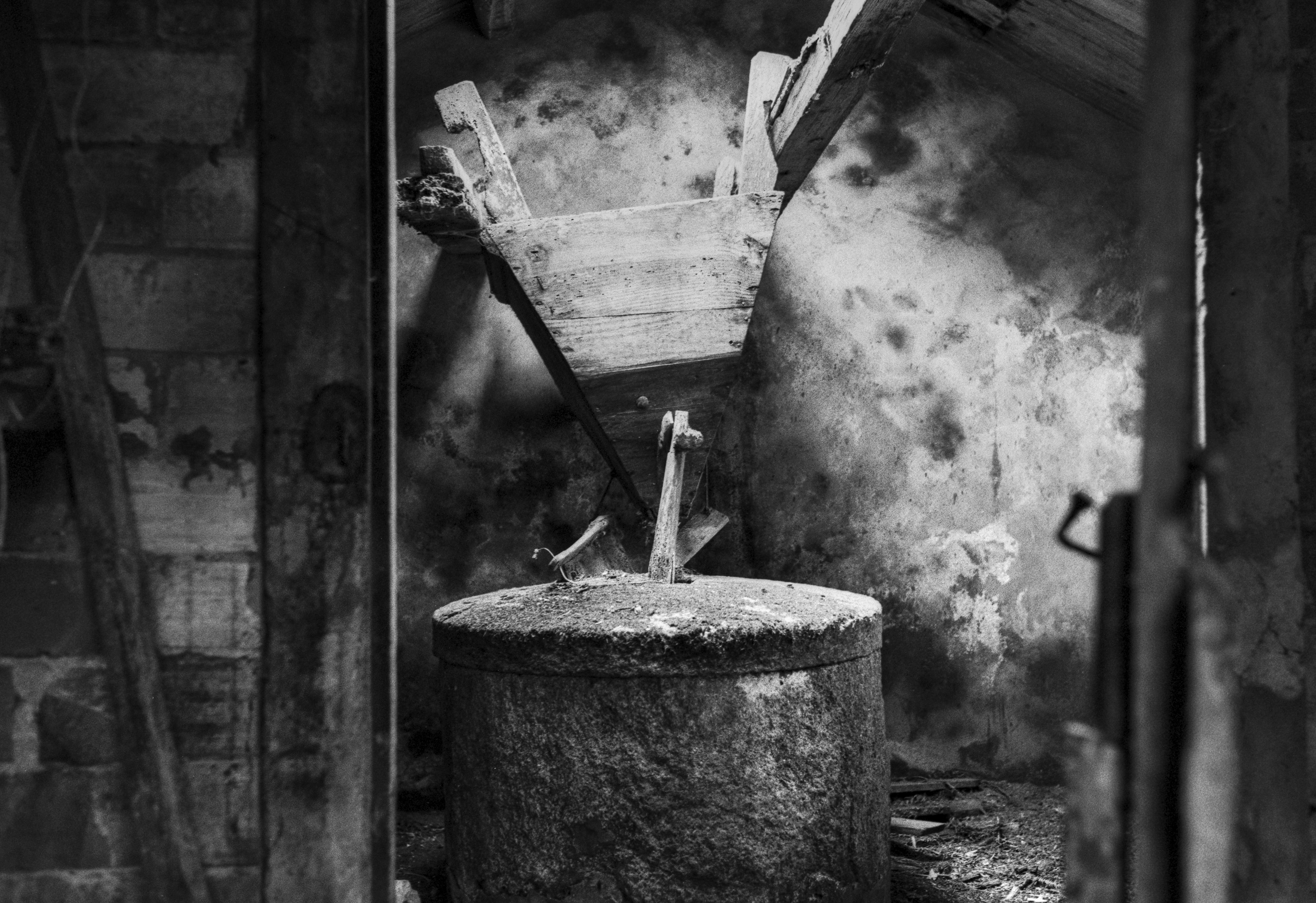 Interior of an old watermill, with a worn millstone and the wooden hopper suspended above it.
