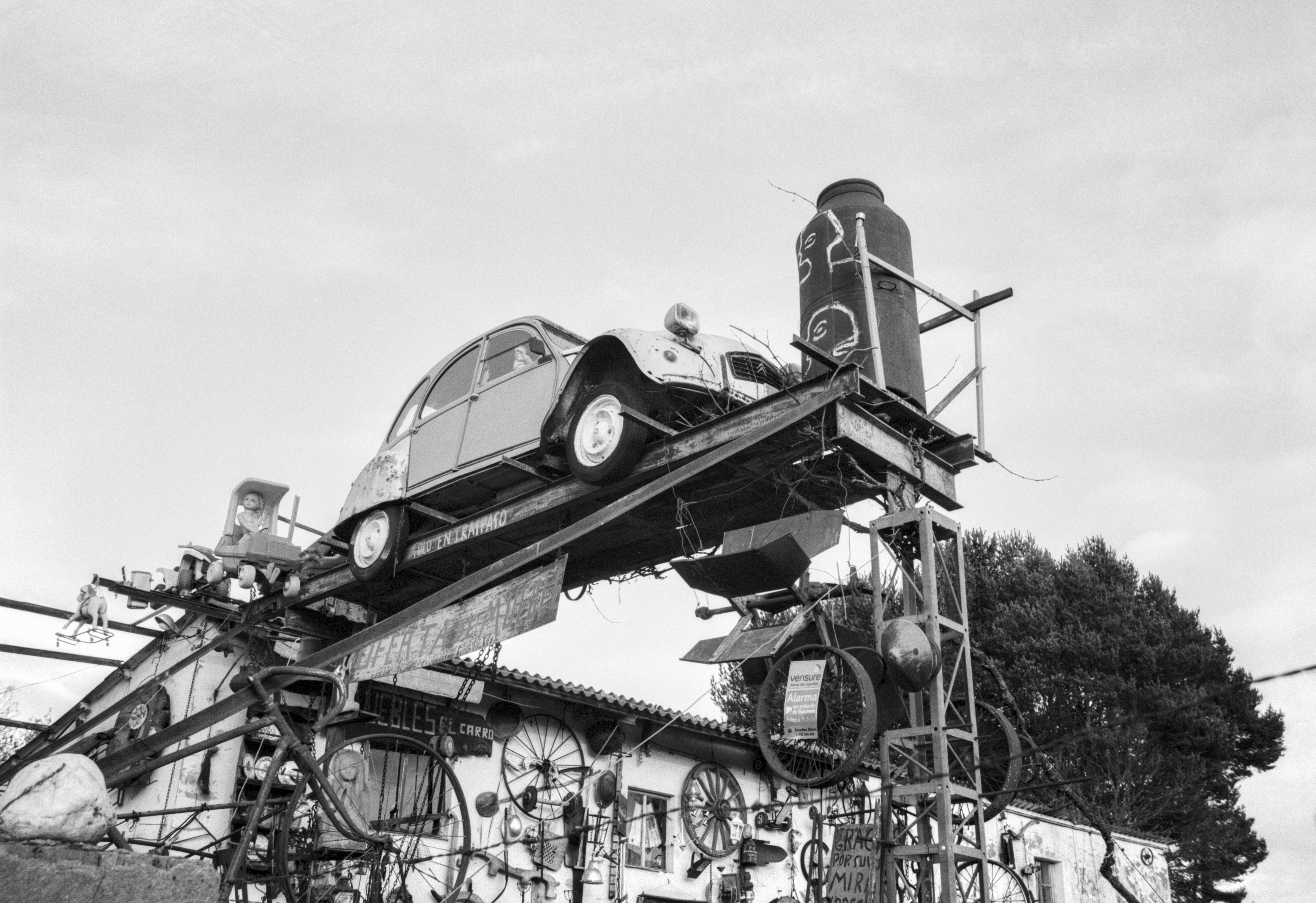 A quirky roadside display in Sanabria featuring an old Citroën 2CV mounted on a metal structure with various objects and wheels.